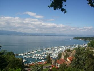 Photo du lac, des maisons et un port de plaisance à l'avant, un horizon légèrement montagneux sur la rive opposée.