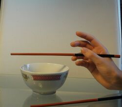Pour tenir des baguettes, il faut commencer par placer celle du dessous dans le creux entre le pouce et l'index et la poser sur l'annulaire.