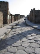 Une rue à Pompéi : voie romaine urbaine dallée, bordée de trottoirs. Ici, les dalles polygonales donnent un rythme aléatoire au choc des roues.