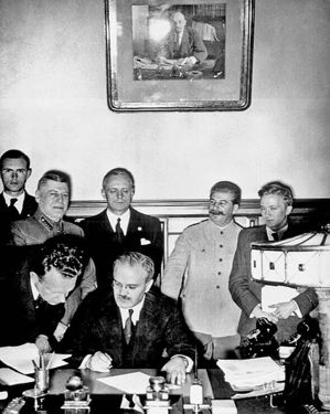 Signature du Pacte de non-agression, Molotov est assis, Ribbentrop est derrière lui, et Staline est à sa gauche.